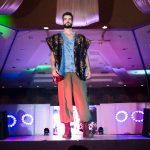 Modelo masculino desfila em uma passarela durante um evento de moda em ambiente interno.