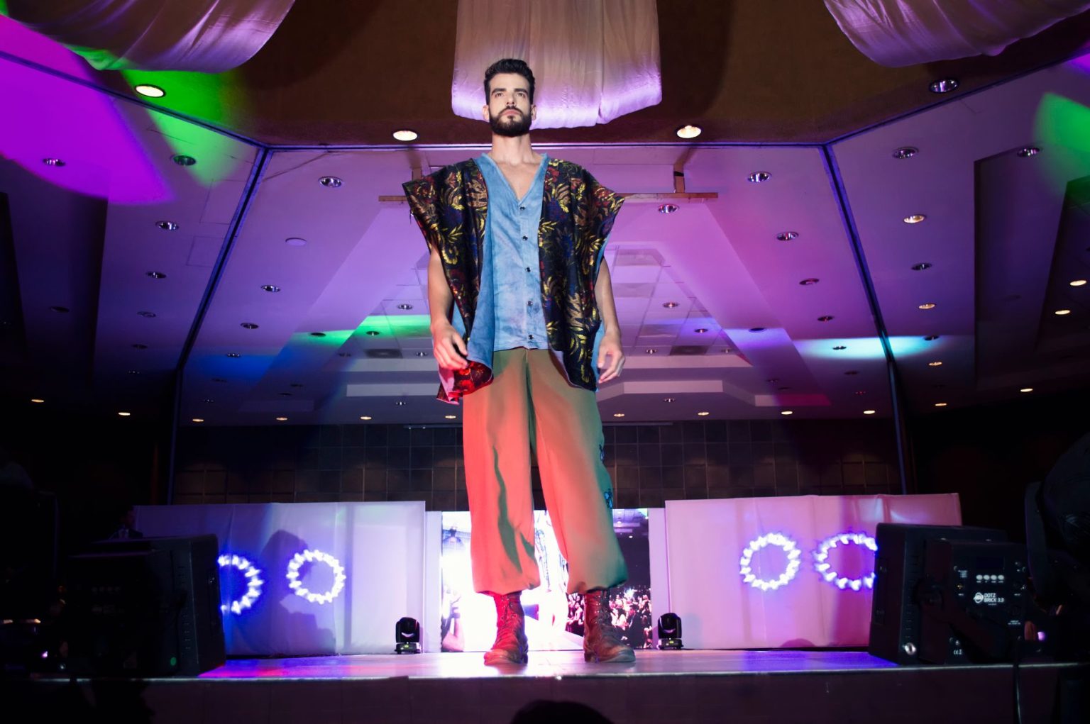 Modelo masculino desfila em uma passarela durante um evento de moda em ambiente interno.