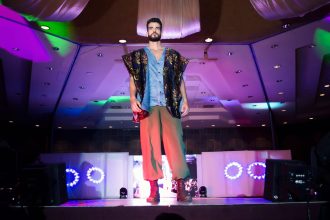 Modelo masculino desfila em uma passarela durante um evento de moda em ambiente interno.