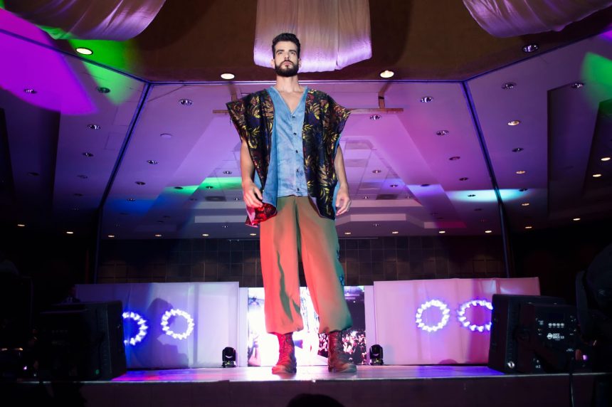 Modelo masculino desfila em uma passarela durante um evento de moda em ambiente interno.