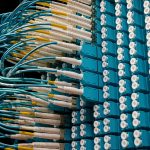 Cabos de fibra óptica conectados a um painel azul em um data center.