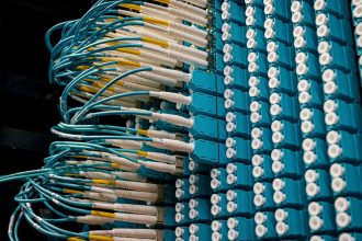 Cabos de fibra óptica conectados a um painel azul em um data center.