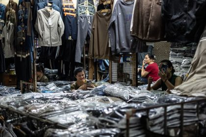 Interior movimentado de uma loja de roupas, com funcionários organizando produtos e cuidando do estoque.