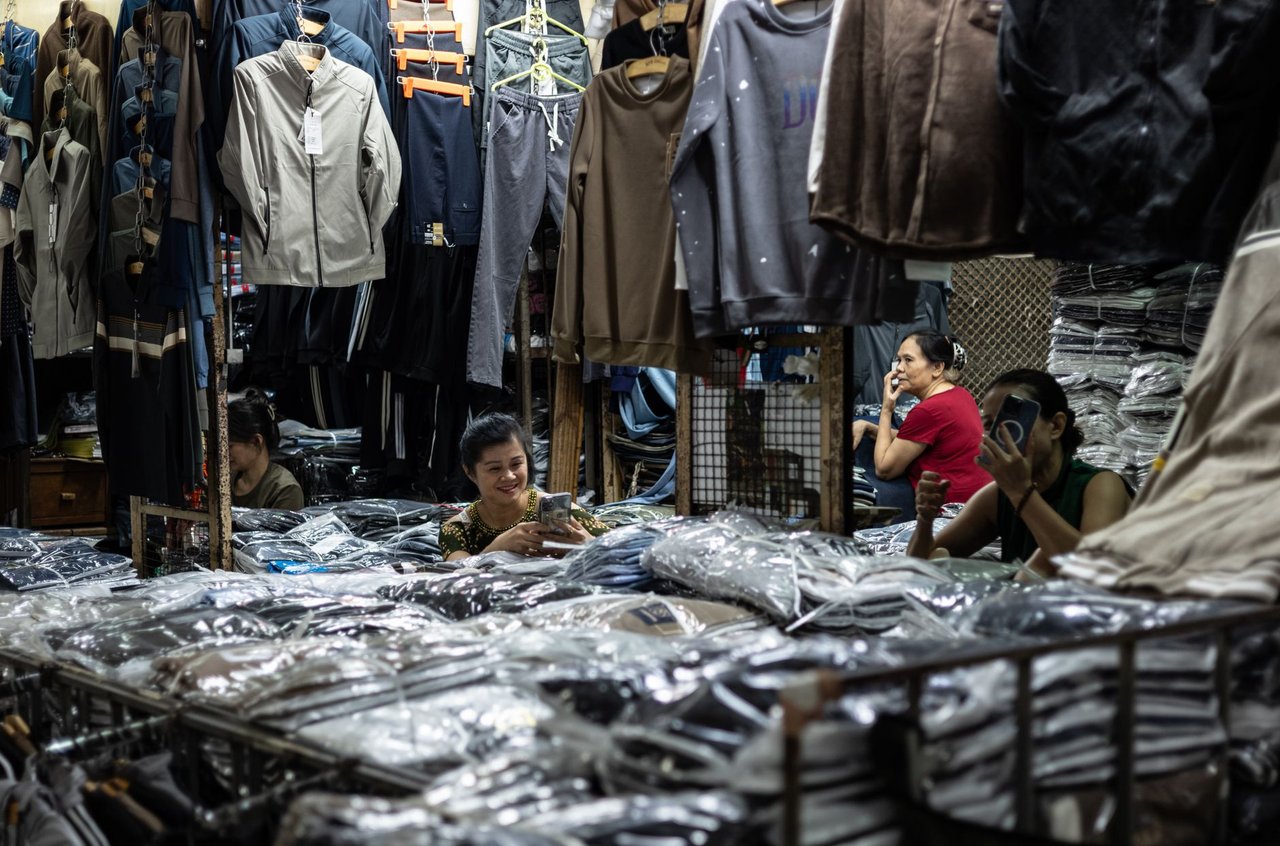Interior movimentado de uma loja de roupas, com funcionários organizando produtos e cuidando do estoque.