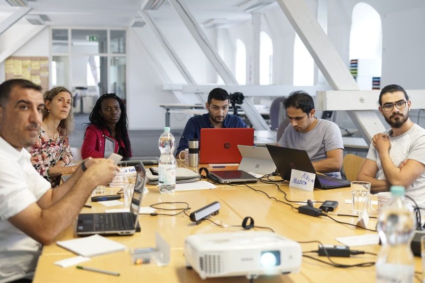 Equipe diversa reúne-se em torno de uma mesa de conferência, usando laptops e discutindo projetos em um escritório moderno.