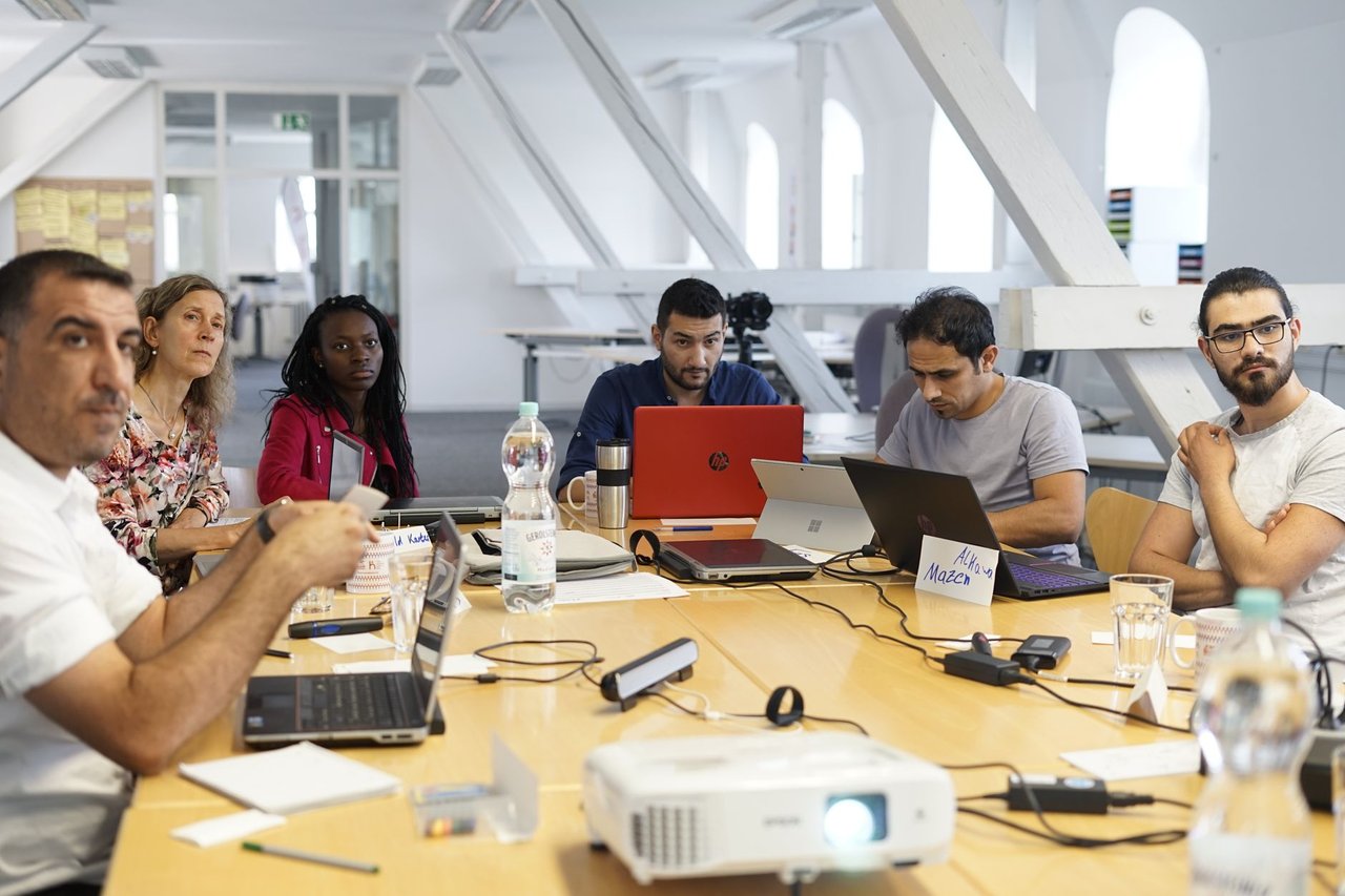Equipe diversa reúne-se em torno de uma mesa de conferência, usando laptops e discutindo projetos em um escritório moderno.