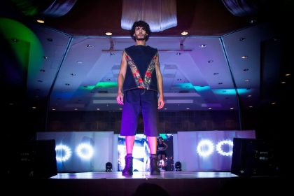 Modelo masculino desfila com um look de moda em uma passarela iluminada.