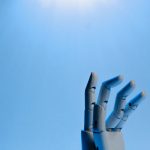 Mão robótica articulada erguida contra um fundo azul, em uma ilustração conceitual sobre inteligência artificial
