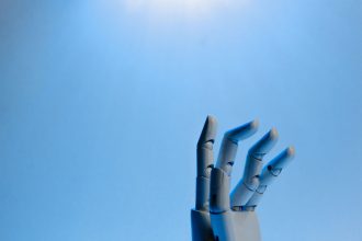 Mão robótica articulada erguida contra um fundo azul, em uma ilustração conceitual sobre inteligência artificial